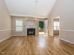 Spacious living room with laminate wood flooring, a fireplace, and two windows. French doors lead to a deck with a view of greenery. Neutral walls and white trim create an airy feel.