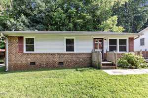 Located at 213 W Westbury Drive, Oxford, this charming single-story brick and white siding house boasts red shutters. It features a small wooden porch and ramp, surrounded by lush green grass and trees in the background.