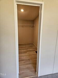 Small empty closet with light wood flooring, cream-colored walls, and a single overhead wire shelf. A light in the ceiling illuminates the space. The doorway has a white frame.