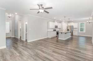 Spacious open-concept kitchen and living area with light gray walls and wood-patterned laminate flooring. The kitchen features white cabinets, stainless steel appliances, an island with pendant lights, and a dining area under a chandelier.
