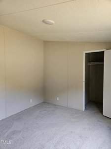 Empty room with light beige walls, a textured ceiling, and a closed white closet door. The carpet is light gray, and there is a ceiling light fixture.