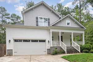 Located in the charming Franklinton area, this two-story house at 3709 Sapphire Court boasts light gray siding with stone accents. It features a two-car garage, a covered porch with white railings, and a sloped concrete driveway. Surrounded by trees, it also offers a manicured front lawn.