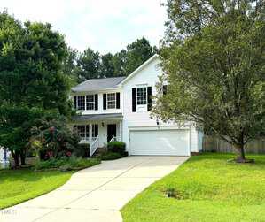 Nestled on 447 Mayview Drive, this two-story white house in Creedmoor boasts a double garage, surrounded by trees and lush greenery. The welcoming front features a quaint porch and multiple windows, with a concrete driveway leading up to the garage under a cloudy sky.