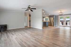 A spacious and bright open-plan living area with light wood flooring. It features a modern kitchen with stainless steel appliances and a stylish light fixture. There's a ceiling fan in the living area and large windows that bring in natural light.