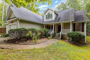 Located in Franklinton, this two-story house at 4104 Elton Circle boasts beige siding, white trim, and a dark gray roof. The inviting front features a porch with steps, surrounded by lush green shrubs and trees. A curved walkway guides you to the entrance, accenting the partially grass-covered yard.