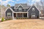 Located at 3996 Cashmere Lane, Youngsville, this modern two-story house boasts dark gray siding and stone accents, complemented by a large front porch. The yard is beautifully landscaped with small shrubs and trees, while the sky above remains partly cloudy.