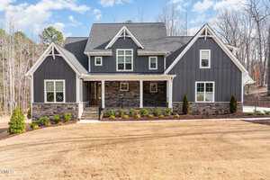 Located at 3996 Cashmere Lane, Youngsville, this modern two-story house boasts dark gray siding and stone accents, complemented by a large front porch. The yard is beautifully landscaped with small shrubs and trees, while the sky above remains partly cloudy.