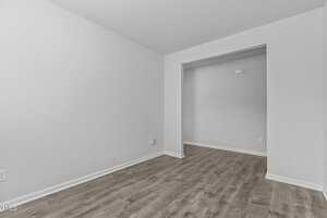 Empty room with light grey walls and wood-style flooring. The room has an open doorway leading to another space, with a minimalist and modern appearance.