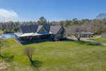 A large house with a gray roof sits on a grassy lawn beside a serene pond in Franklinton. Nearby, at 1641 State Hwy 96, stands a smaller building surrounded by trees and clear blue sky. A paved path gracefully leads to the main house.