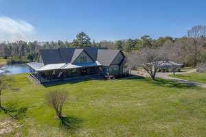 A large house with a gray roof sits on a grassy lawn beside a serene pond in Franklinton. Nearby, at 1641 State Hwy 96, stands a smaller building surrounded by trees and clear blue sky. A paved path gracefully leads to the main house.
