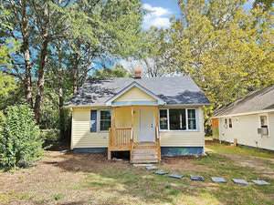 Nestled among trees, the small yellow house at 505 Granville Street features a dark roof and a welcoming front porch. Steps lead to its entrance, while a stepping stone path meanders through the yard toward an adjacent building. A touch of Oxford charm graces this cozy home.