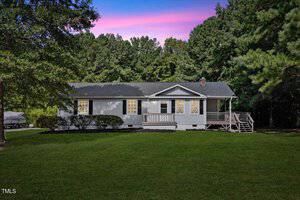 The single-story gray house at 5027 Dorsey Road features a small porch set against a backdrop of trees under a vibrant sunset sky. Its well-maintained lawn is lush and green, with a boat parked to the side, reflecting the charming essence of this Oxford locale.