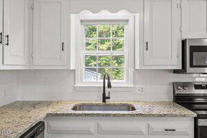 A bright kitchen features white cabinets, a speckled granite countertop, and a stainless steel oven and microwave. A black faucet sits over the sink beneath a window with a view of green trees.