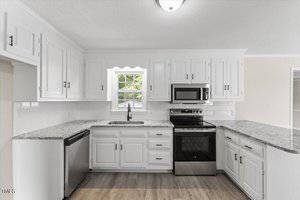 A bright kitchen with white cabinets and a granite countertop. It features a stainless steel oven, microwave, and dishwasher. A window above the sink lets in natural light, and the floor is light wood.