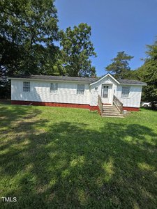 A small, single-story white house with a red brick foundation sits at 4547 S US Hwy 15. Set against a backdrop of trees, the charming Oxford residence features a front porch with steps leading to the entrance and is situated in a grassy yard under a clear blue sky.