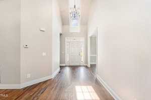 A bright and spacious entryway with high ceilings, featuring wooden floors and a large chandelier. Sunlight streams in through a window above the front door, illuminating the neutral-toned walls and creating a welcoming atmosphere.