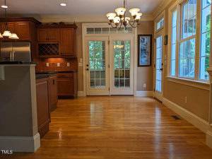 Spacious kitchen with hardwood floors, wooden cabinets, a stainless steel refrigerator, and French doors leading to a screened porch. Large windows on the right side let in natural light. A chandelier hangs from the ceiling.