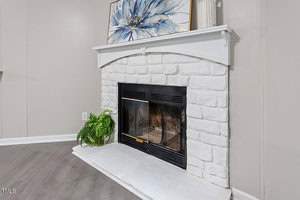 A white stone fireplace with a black metal screen, topped with decorative items including a blue and white abstract painting and vases. A green fern sits on the hearth. The wall and flooring are neutral toned.