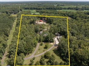Aerial view of the large wooded property at 6200 Cricket Creek Lane, outlined in yellow. The Oxford area includes a house, a pool, and other structures nestled among dense trees. A winding driveway leads to the main house, with the lush green landscape stretching beyond.