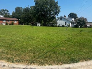 A grassy residential lot on Oxford's serene 48 & 49 Peace Street features a few trees in the background and a charming house to the right. The sky is clear and blue, creating a peaceful atmosphere.
