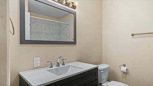 A bathroom with a white countertop, silver faucet, and dark cabinet. A large mirror is above the sink, and a toilet is to the right. The shower with a marble-patterned wall is reflected in the mirror. A towel bar is on the wall.