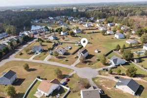 Aerial view of a suburban neighborhood with scattered houses, trees, and a water tower in the background. A location pin highlights one of the houses, marking its significance. The landscape is slightly hilly with autumn-colored foliage.