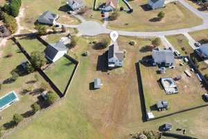 Aerial view of a suburban neighborhood with several houses on spacious plots of land. The image shows a cul-de-sac with homes surrounded by grass and trees. A location pin marks one of the houses centrally in the image.