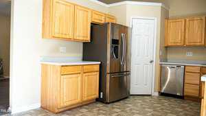 Kitchen with light wood cabinets, stainless steel refrigerator, and dishwasher. Beige walls and tiled floor. White door to pantry. Neutral and modern design.