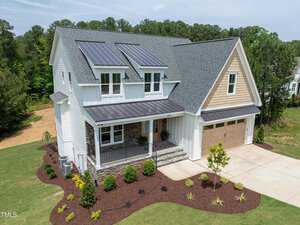 Located at 3991 Hope Valley Drive in the scenic Wake Forest area, this modern two-story house boasts solar panels on the roof. With white siding and stone accents, it includes a two-car garage, covered porch, and a landscaped front yard framed by neatly trimmed hedges and lush greenery.