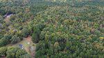 Aerial view of a dense forest near Oxford, with a mix of green and autumn-hued trees. A small house and a red-roofed shed at 8199 Highway 96 N sit in a clearing at the bottom left corner. The rest of the image is filled with lush trees extending into the distance.