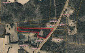 Aerial view of a rural area featuring a section of land outlined in red. Multiple parcels of land are labeled with addresses such as "9515 NC HWY 49" along the highway. The surrounding area includes trees, open fields, and small bodies of water.