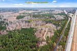 Aerial view of 3100 Knotts Grove Road, Oxford, with an estimated property boundary outlined in yellow. A road runs along the right side with a few vehicles visible. The landscape consists of dense trees and distant fields under a partly cloudy sky.