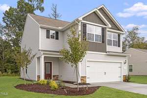 Located at 702 Rhino Bend in Oxford, this two-story house features elegant gray siding with white trim and brown accents. It boasts a spacious white double garage door, a cozy porch, and a landscaped front yard with young trees and shrubs, all set against a backdrop of clear skies and distant trees.