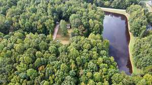 Aerial view of a forested area with a small house and driveway at 1524 Dogwood Drive in the center. A large pond, bordered by trees, is seen on the right near Oxford, with a narrow road running alongside it.