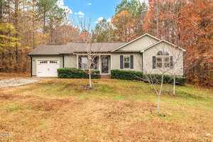 Located at 2221 Irvin Street in Oxford, this charming one-story house features light siding and a dark roof. A single-car garage complements the large window. Surrounded by trees with autumn foliage under a partly cloudy sky, a lush grassy lawn welcomes you home.