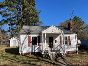 A small, charming white house with red shutters and a chimney sits cozily at 306 Coleman Street in Oxford. Surrounded by trees, it boasts a porch with steps leading to the front door and an antenna perched on the roof. A bright grassy yard and a white shed complete this picturesque setting.