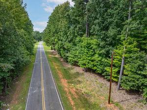A straight, two-lane road flanked by dense green trees stretches into the distance. The sky is partly cloudy. A utility pole is visible on the right side of the road.