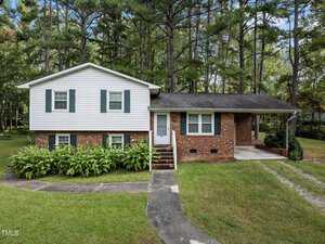 At 129 Maluli Drive in Oxford, this split-level house boasts a charming brick and white siding exterior, nestled among tall trees and bushes. A small set of stairs guides you to the front door, while a neatly cut lawn complements the driveway on the right.