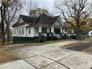 Nestled at 202 Forest Avenue, this large, older white house with a dark roof boasts a spacious front porch. Elevated with steps and a ramp on the right, it overlooks trees with sparse leaves. A concrete driveway and walkway accentuate its charming Oxford-like appeal.