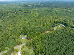 Aerial view of a densely forested landscape near Oxford, with patches of open land. A winding road, 0000 Reavis Road, cuts through the greenery, with a few houses visible nearby. The horizon reveals more trees and distant fields under a clear sky.