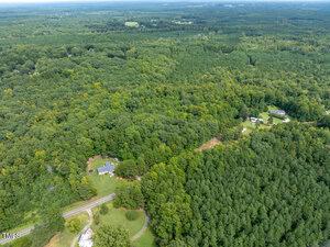Aerial view of a densely forested landscape near Oxford, with patches of open land. A winding road, 0000 Reavis Road, cuts through the greenery, with a few houses visible nearby. The horizon reveals more trees and distant fields under a clear sky.