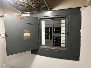 An open electrical panel with multiple circuit breakers is mounted on a white wall. The panel door, which is labeled and marked with the number "54F5," is swung open.