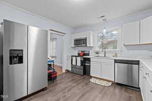 A modern kitchen with stainless steel appliances, including a refrigerator, oven, and dishwasher. White cabinets and a marble-patterned countertop complement the light blue walls. A window above the sink lets in natural light.