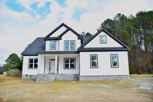 Set against a backdrop of trees in Franklinton, this newly constructed two-story house at 1586 Nc 96 Hwy features a combination of dark and light exterior trim, large windows, a covered front porch, and an elegant stone facade under a partly cloudy sky.