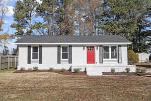 Located at 124 W College Street, this single-story white brick house in Oxford features a striking black roof and elegant black shutters. Its prominent red front door welcomes visitors to a charming porch, steps away from a lush grassy lawn, with a wooden fence elegantly lining the left side.