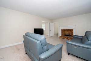 A living room with two blue leather sofas facing a flat-screen TV. There's a brick fireplace on the right, and an open door leading to another room. The carpet is light-colored, and the walls are off-white.