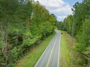 A winding road runs through a forested area with dense trees on both sides. A red car is parked on the right side of the road. The sky is partly cloudy, and the scene suggests a calm, scenic drive through nature.