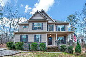 Located at 2499 Golden Forest Drive in Franklinton, this charming two-story house features tan siding and stone accents on the lower half. An American flag graces the front porch, while neatly trimmed bushes and a small tree adorn the yard, set against a backdrop of tall trees under a partly cloudy sky.