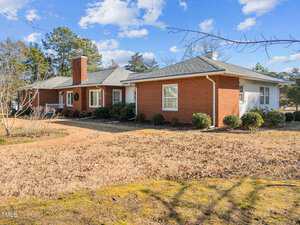 Nestled on 216 W Thorndale Street, this single-story brick house in Oxford features a chimney and white trim. It boasts a gabled roof and cozy porch, while the yard is dotted with dry grass and shrubs. A pathway leads to the entrance, surrounded by trees under a partly cloudy sky.