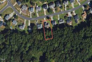 Aerial view of a neighborhood with several houses on a curved street named Rodgers Pt. One house, located at 1610 Rogers Pointe Lane, is outlined in red, highlighting its proximity to a wooded area. The lush surroundings include manicured lawns and winding driveways in the charming Creedmoor community.